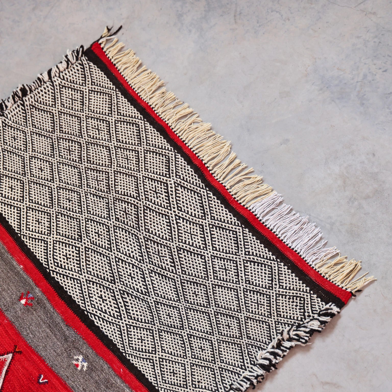 Textile with geometric pattern and fringes on a gray surface