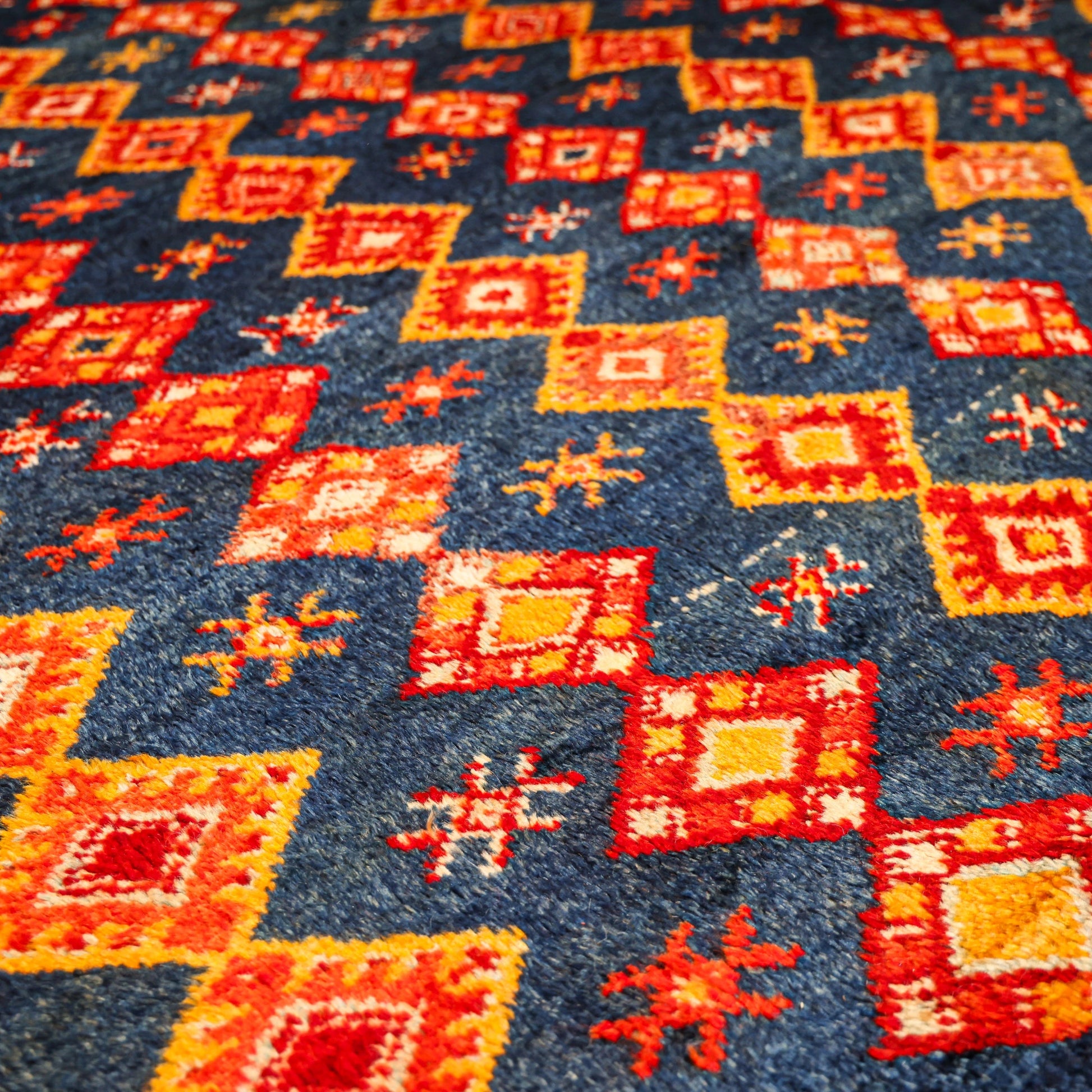 Close-up of a patterned carpet with red, orange, and blue geometric designs.
