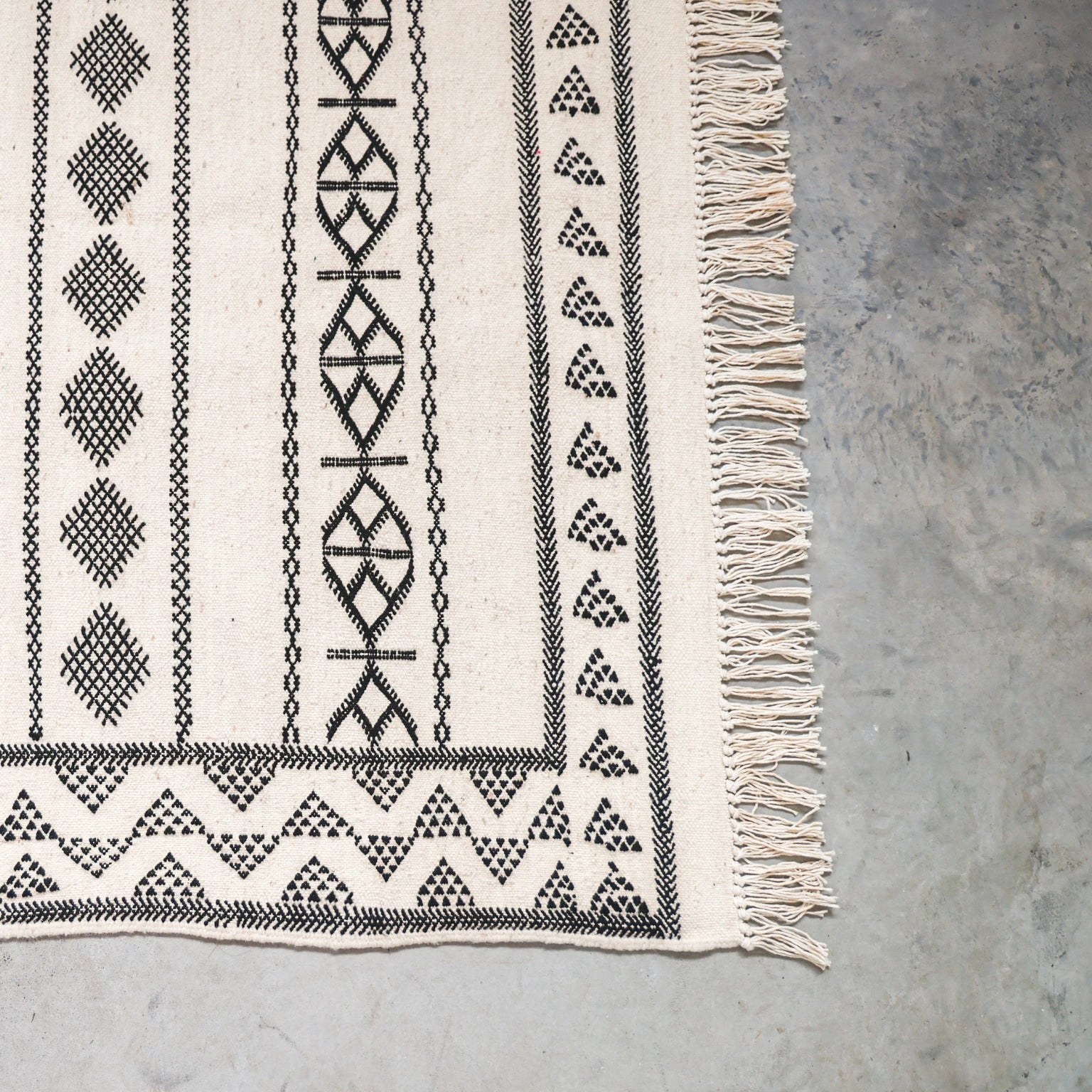 Textile with geometric patterns and fringes on a concrete surface