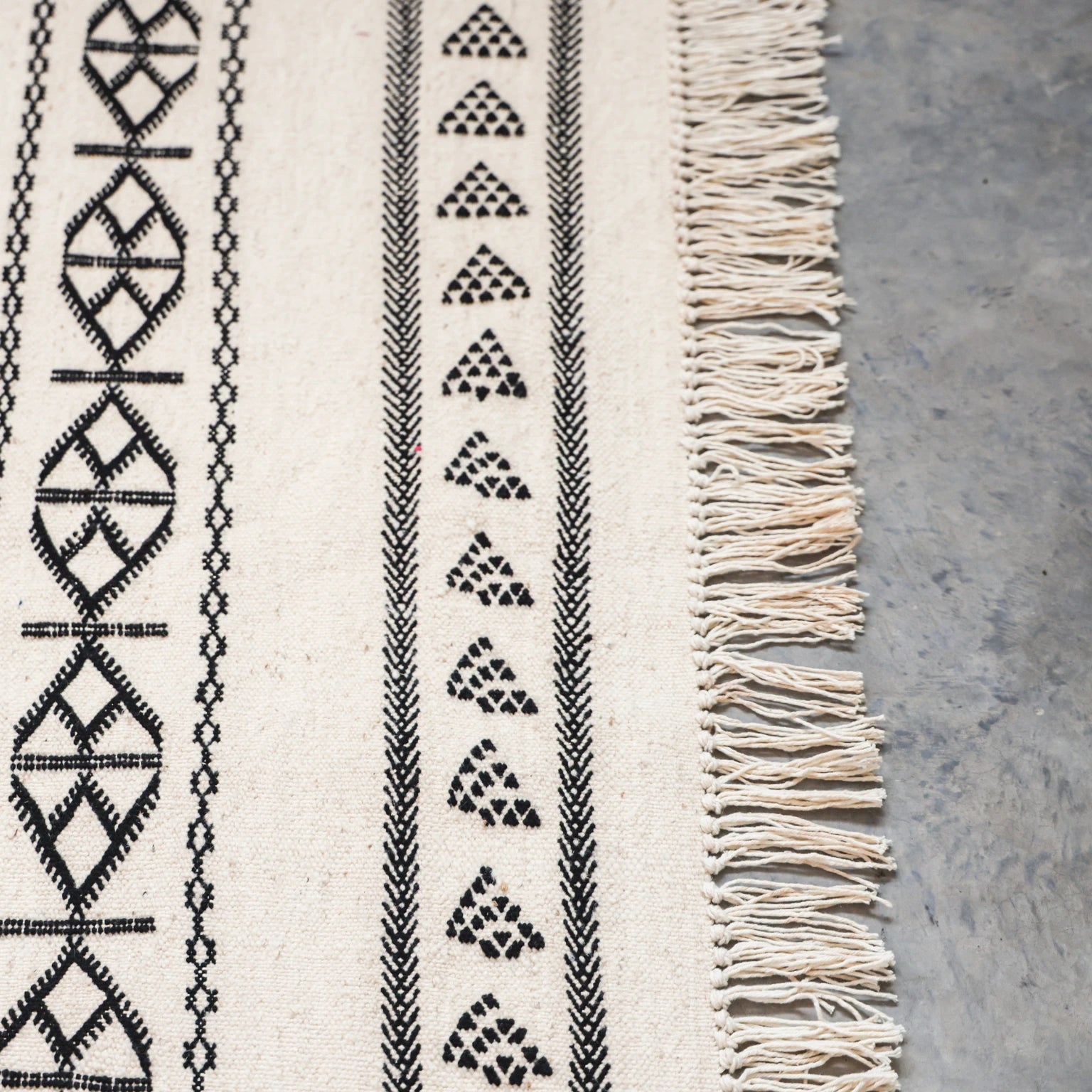 Textile with geometric patterns and fringes on a concrete surface