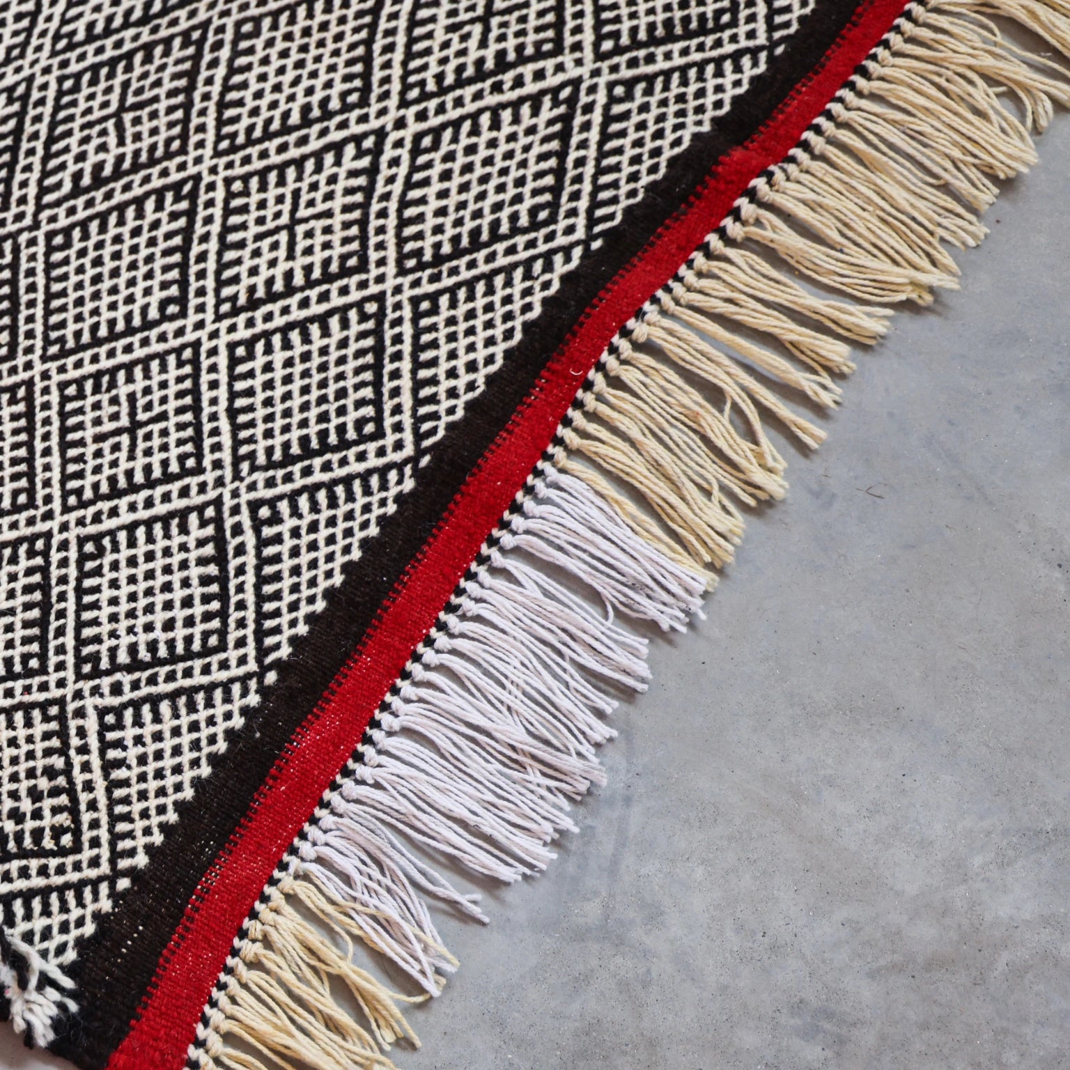 Textile with geometric pattern and fringes on a concrete surface